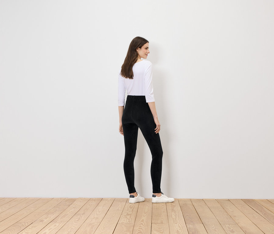 Frau in schwarzen Leggings und weißem Oberteil steht mit dem Rücken zur Kamera.