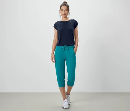 Frau steht mit Händen in den Taschen der türkisen 3/4-Sweathose.