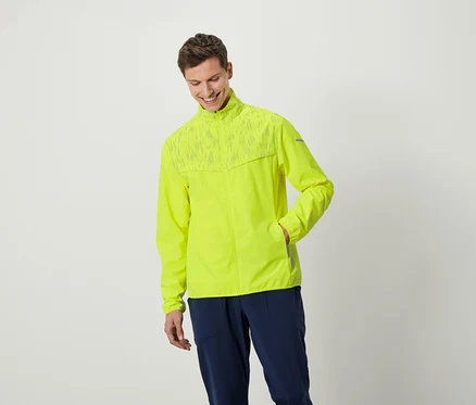 Ein lächelnder Mann posiert in einer neongelben Jacke und dunkelblauen Hosen.