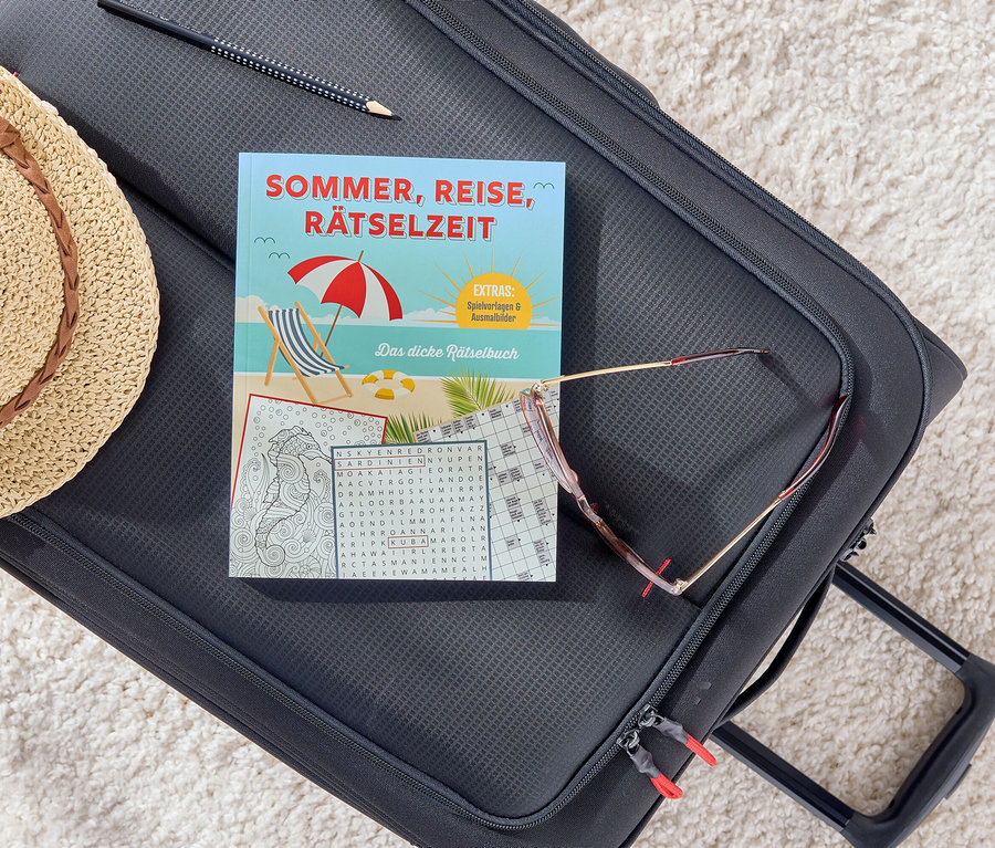 Auf einem schwarzen Koffer liegen ein Buch mit dem Titel Sommer, Reise, Rätselzeit, eine Sonnenbrille, ein Bleistift und ein Strohhut.