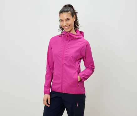 Frau mit hochgesteckten Haaren, die eine pinkfarbene Jacke mit Kapuze und marineblaue Hosen trägt und in die Kamera lächelt.