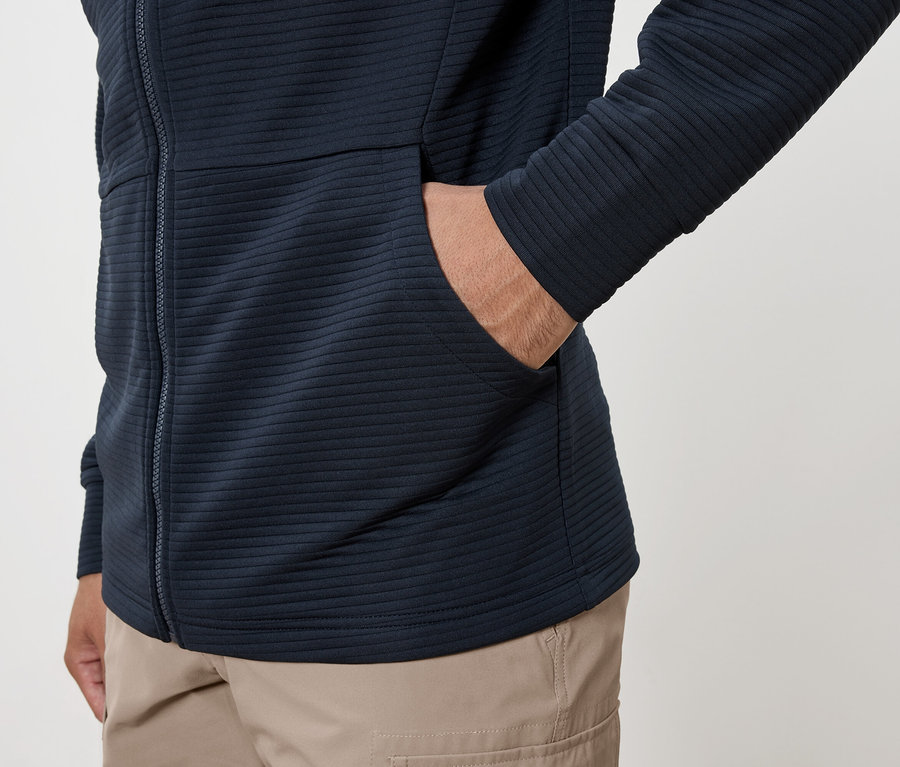 Mann mit Hand in der Tasche einer marineblauen Kapuzenjacke, dazu Cargohose.
