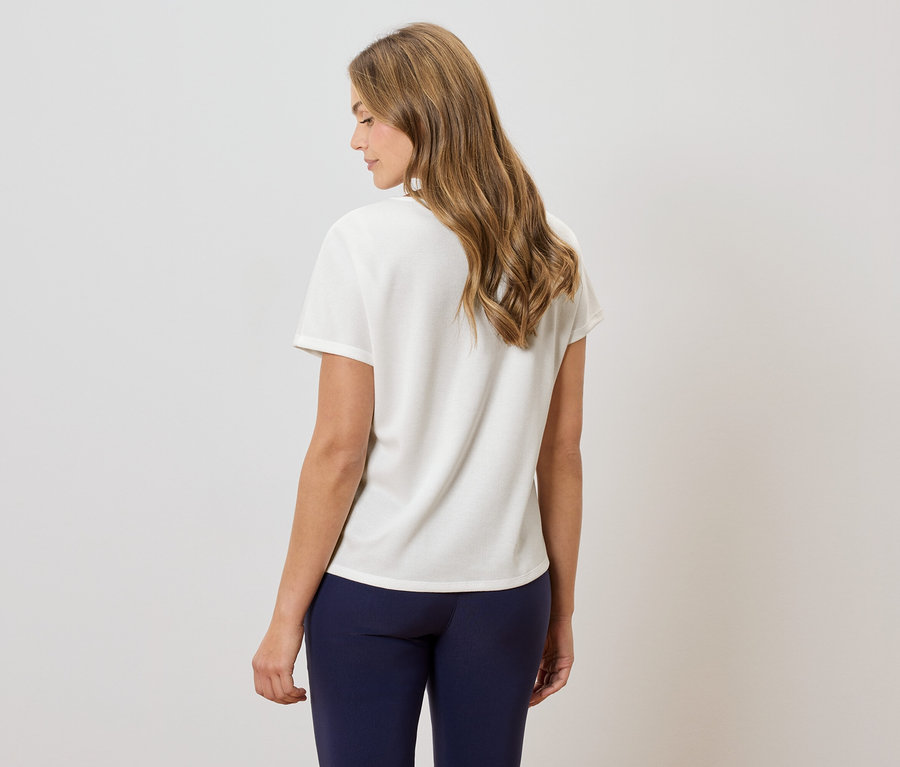 Rückansicht einer Frau mit gewelltem, schulterlangem Haar, die ein cremefarbenes T-Shirt und marineblaue Leggings trägt.