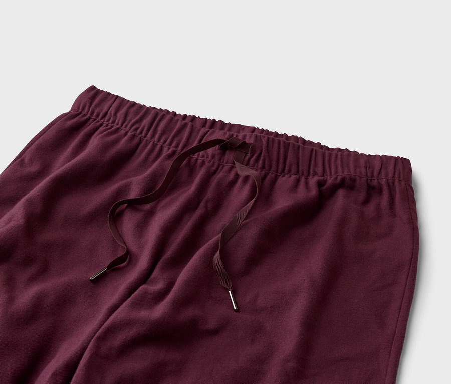 Nahaufnahme einer weinroten Hose mit Kordelzug und Gummibund vor einem hellgrauen Hintergrund.
