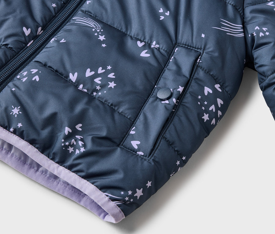 Nahaufnahme einer marineblauen, gesteppten Jacke mit Reißverschluss und lila Akzenten, verziert mit Sternen, Herzen und Kometen.
