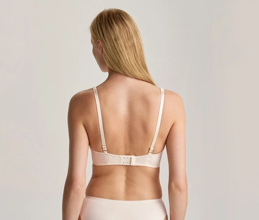 Frau von hinten, trägt einen hellen BH und Slip. Ihr langes blondes Haar fällt über den Rücken.
