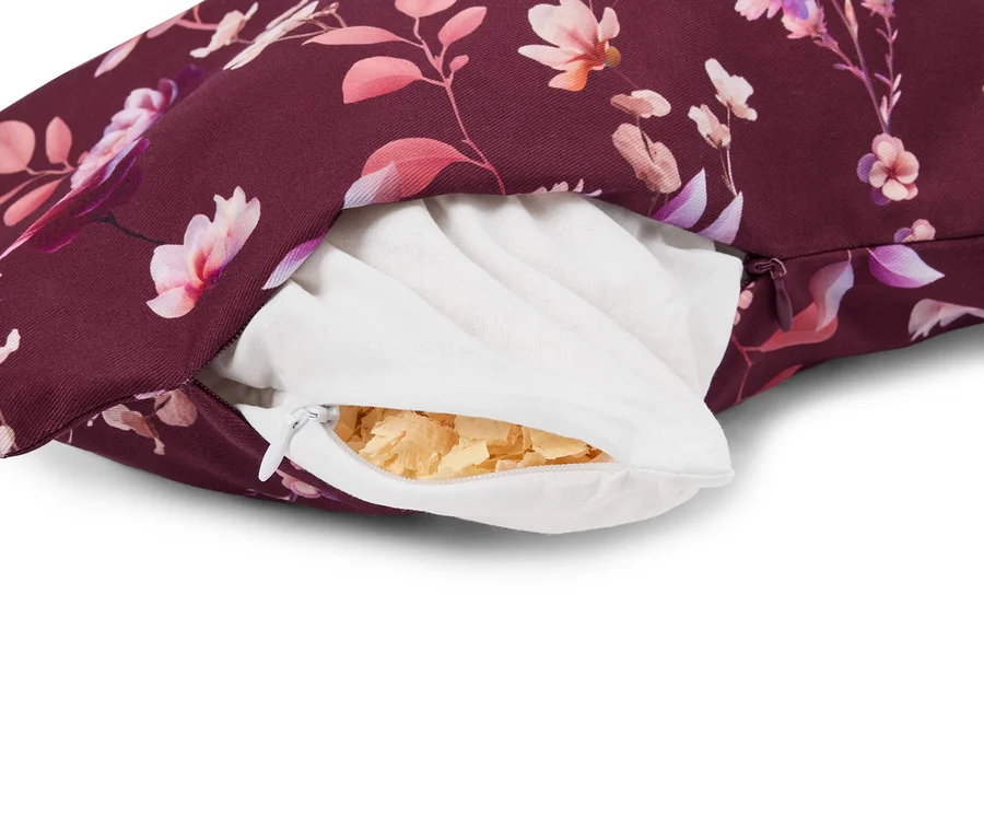 Nahaufnahme eines geöffneten Kissens mit dunkelrotem Blumenmuster, das eine weiße Innenhülle und helle Holzspäne als Füllung zeigt.