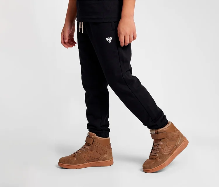 Unterkörper einer Person in schwarzen Jogginghosen und braunen hummel® Sneakern »St Power Play Mid Wt Jr«.