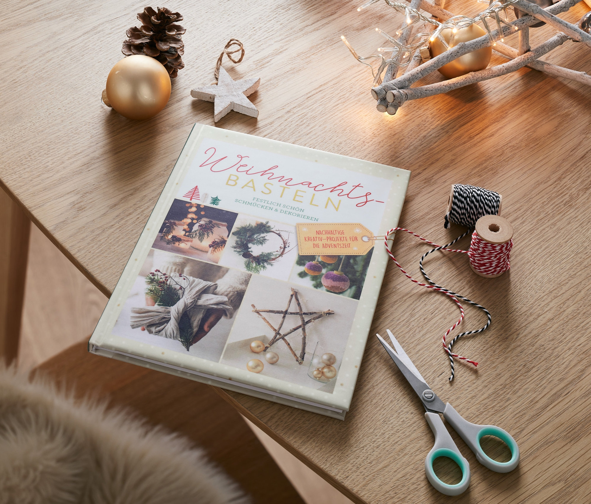 Buch »Weihnachtsbasteln« liegt auf einem Tisch neben einer Schere, Schnüren und Weihnachtsdeko.