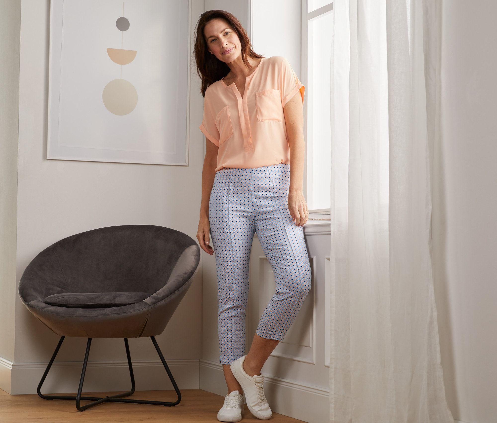 Frau posiert am Fenster, trägt eine bedruckte 7/8-Stretchhose.