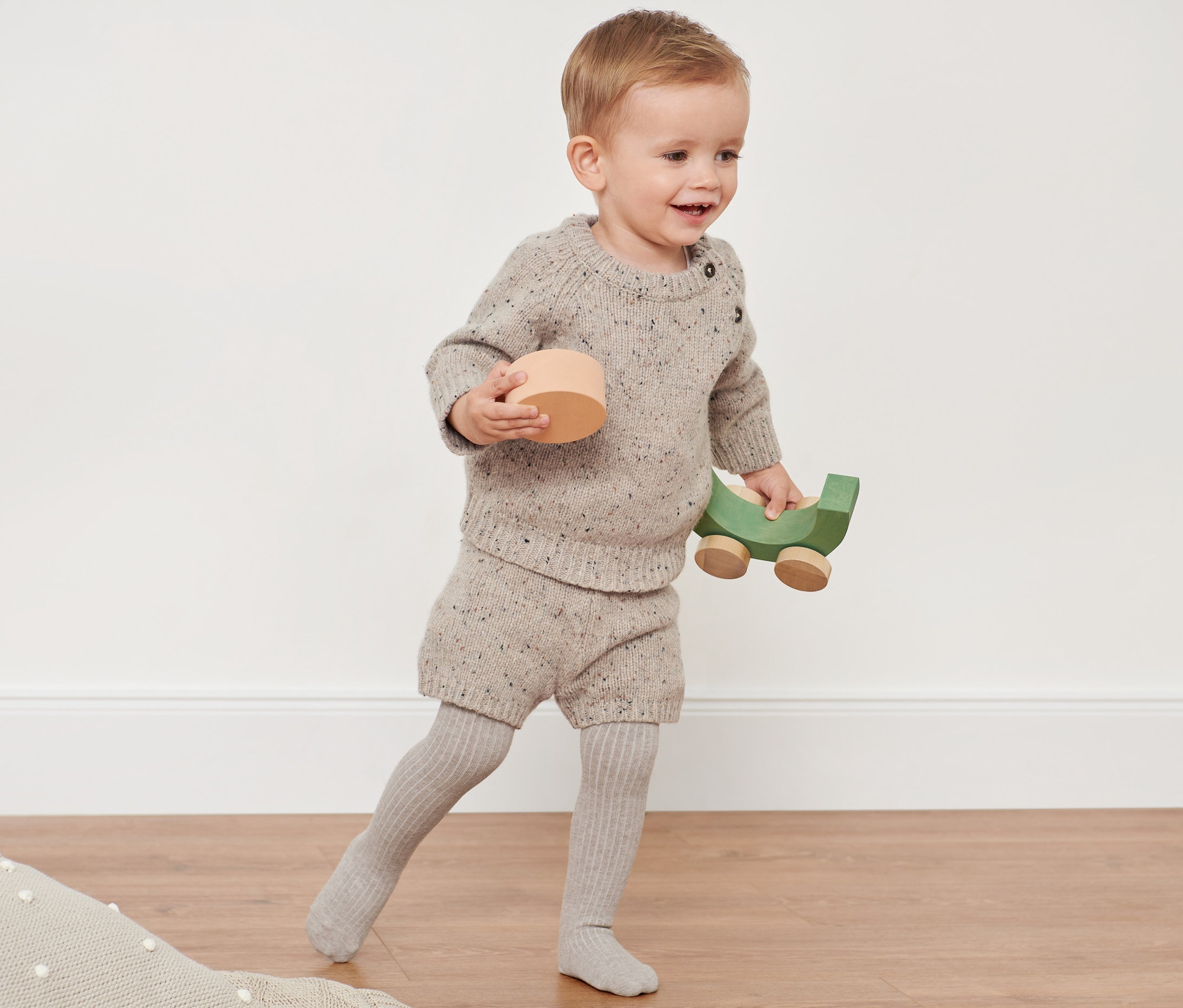 Kleinkind spielt mit Holzspielzeug und trägt eine Strickkombi mit RWS-Wolle.