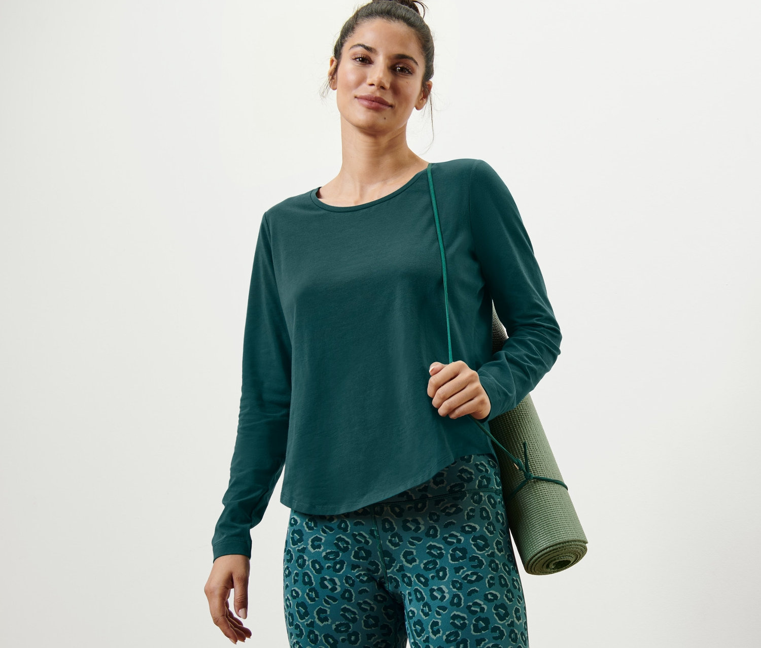 Frau trägt ein grünes Langarm-Sportshirt und eine grüne Yogamatte.