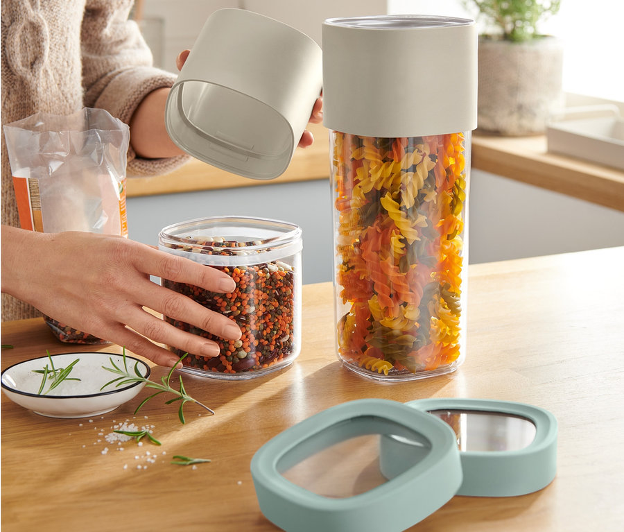 Frau hält geöffnete variable Vorratsdose neben einer mit bunten Nudeln gefüllten Dose.