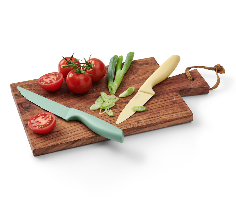 Zwei Küchenmesser aus dem Küchenmesser-Set liegen auf einem Holzbrett mit Tomaten und Frühlingszwiebeln.