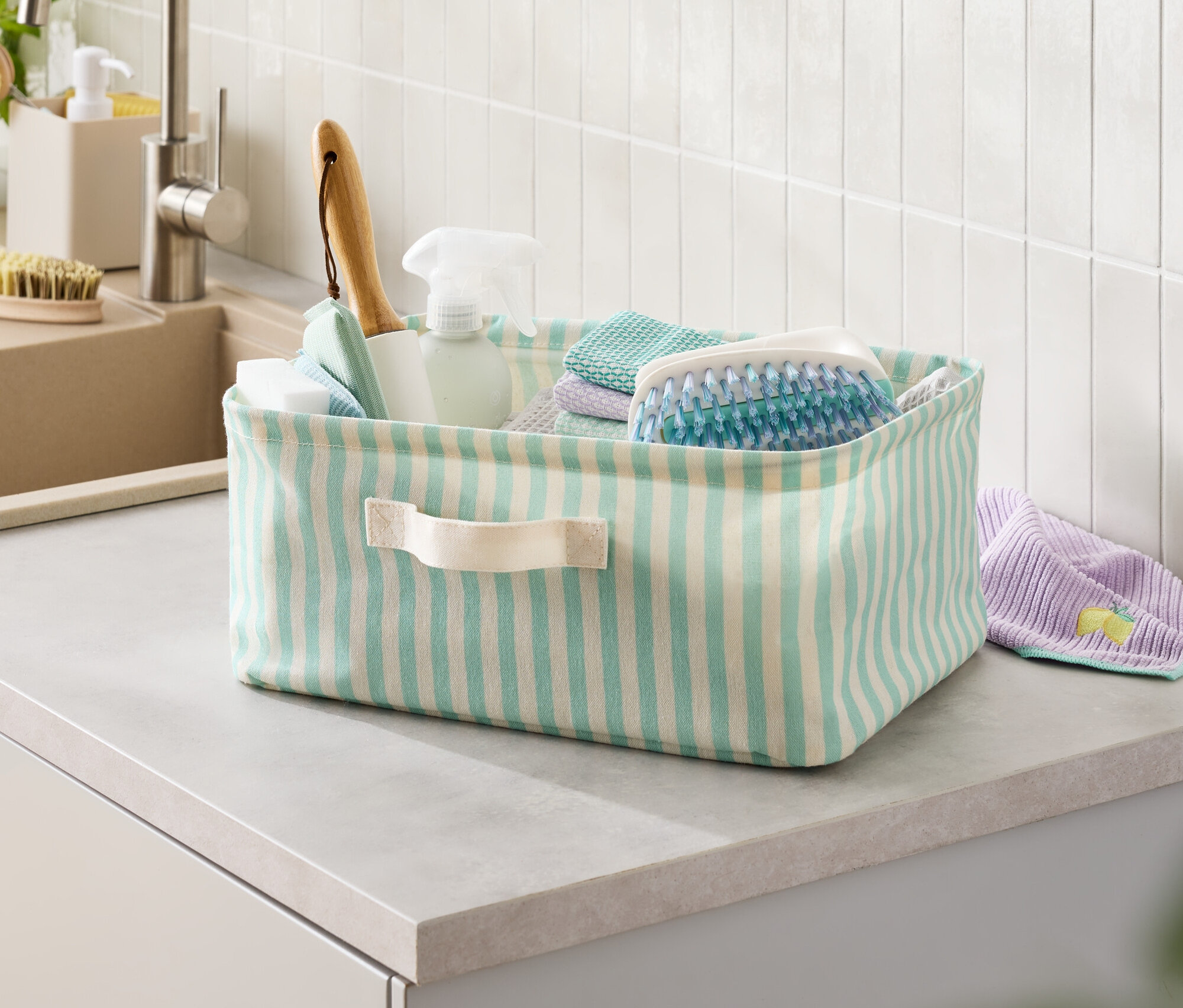 Gestreifter Korb mit Reinigungsmitteln auf der Arbeitsfläche.