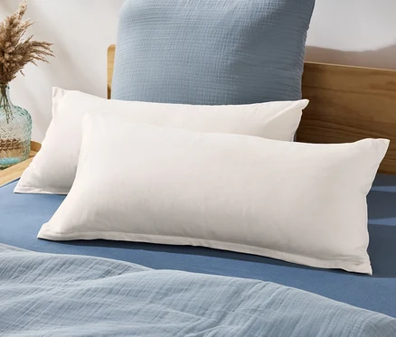 Zwei Jersey-Kopfkissenbezüge liegen auf einem Bett mit blauem Bettlaken und Bettdecke.