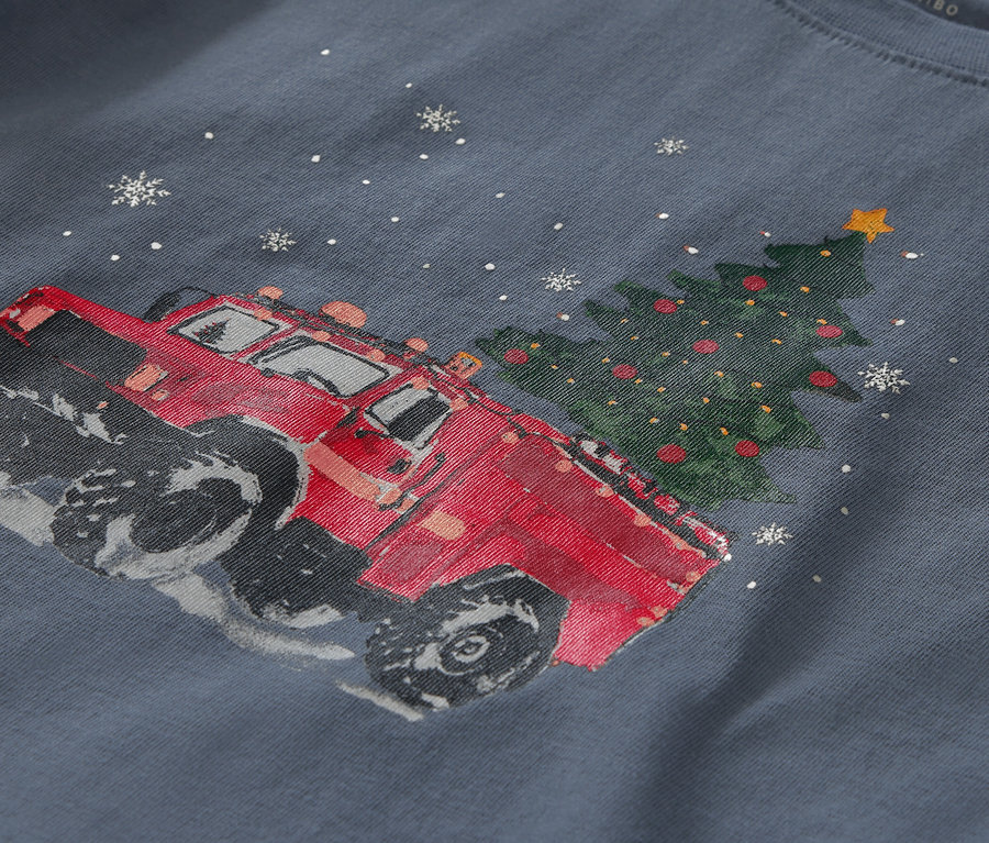 Detailaufnahme eines blauen T-Shirts mit einem Aufdruck eines roten Autos neben einem Weihnachtsbaum und Schneeflocken.