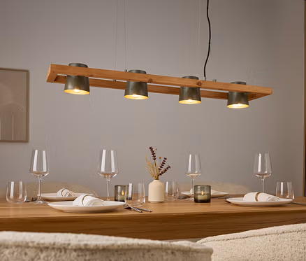 Vier graue Lampen über einem Holztisch mit Gedecken und Gläsern.