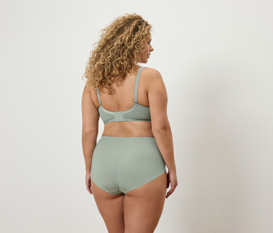 Frau mit lockigem Haar steht mit dem Rücken zum Betrachter und trägt einen hellgrünen BH und Höschen.