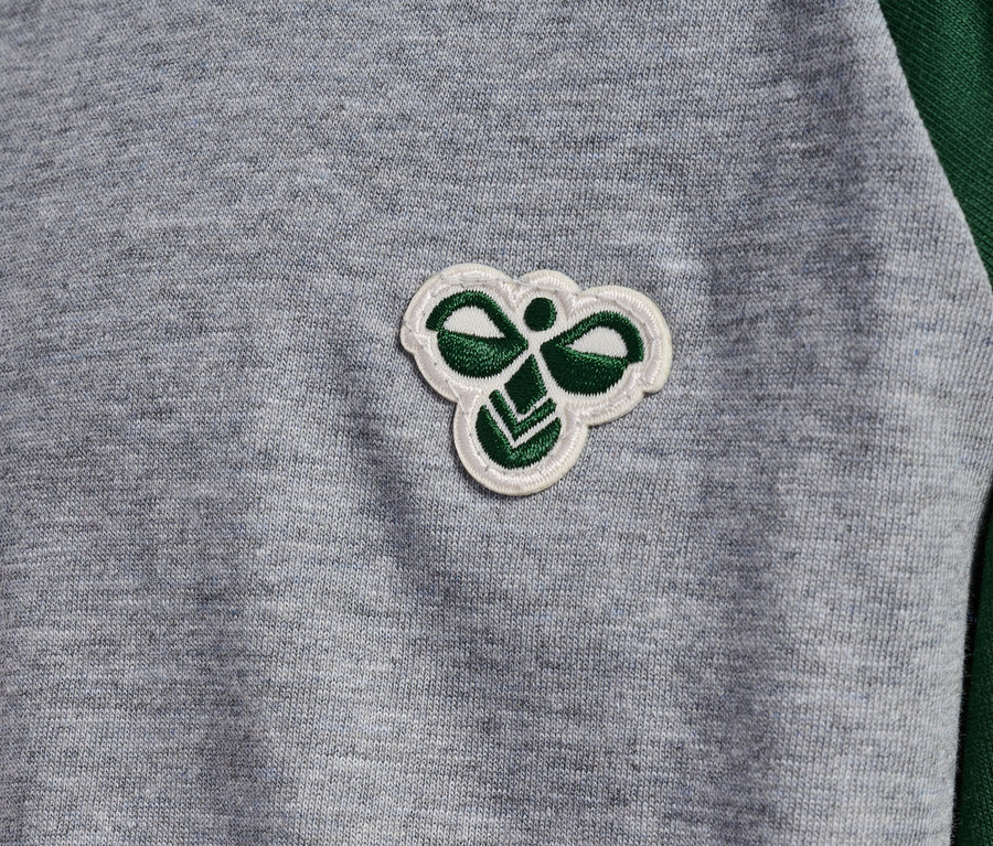 Detailaufnahme eines grauen T-Shirts mit grünen Raglanärmeln und Hummel-Logo.