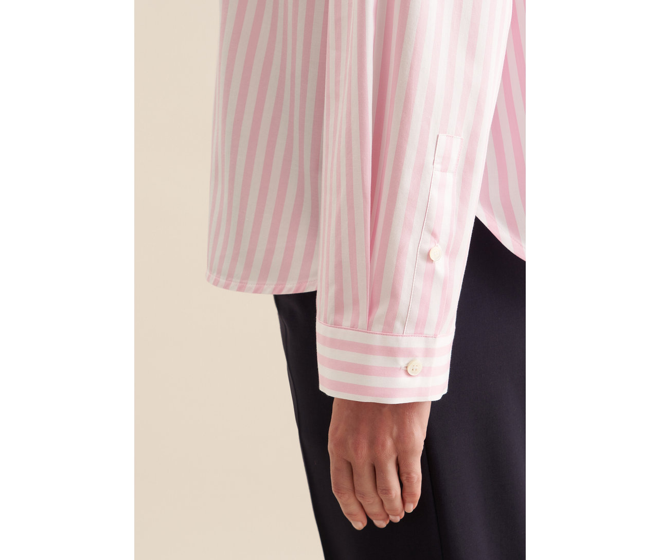 Nahaufnahme eines Arms und einer Hand, die eine roséfarbene, gestreifte Seidensticker Oversize Hemdbluse trägt.