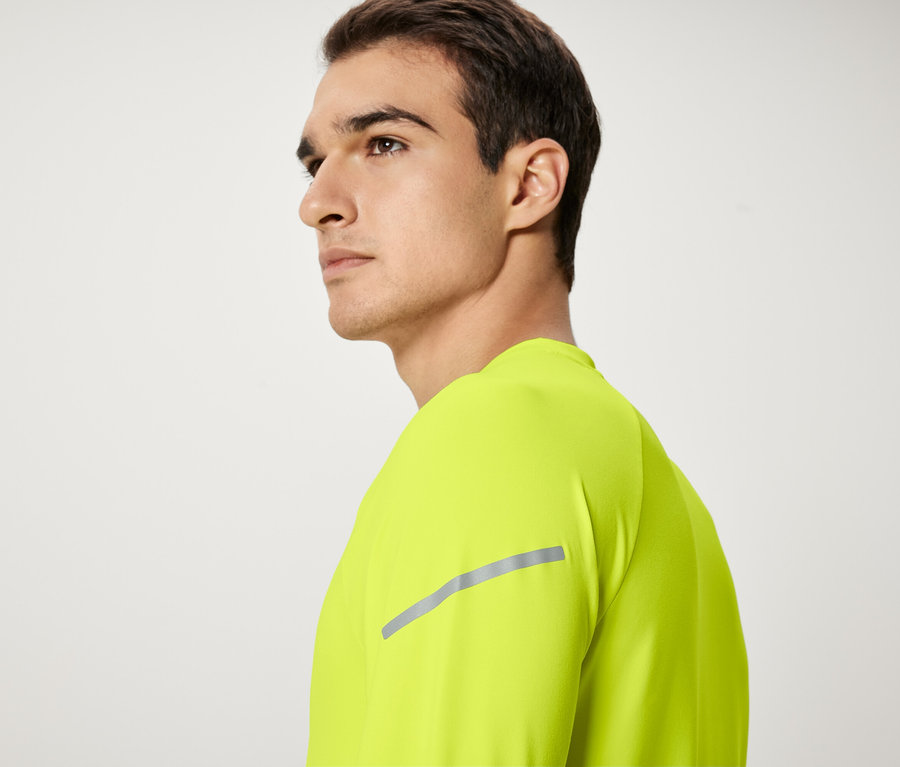 Ein Mann mit braunen Haaren und einem neongelben T-Shirt schaut nach links.