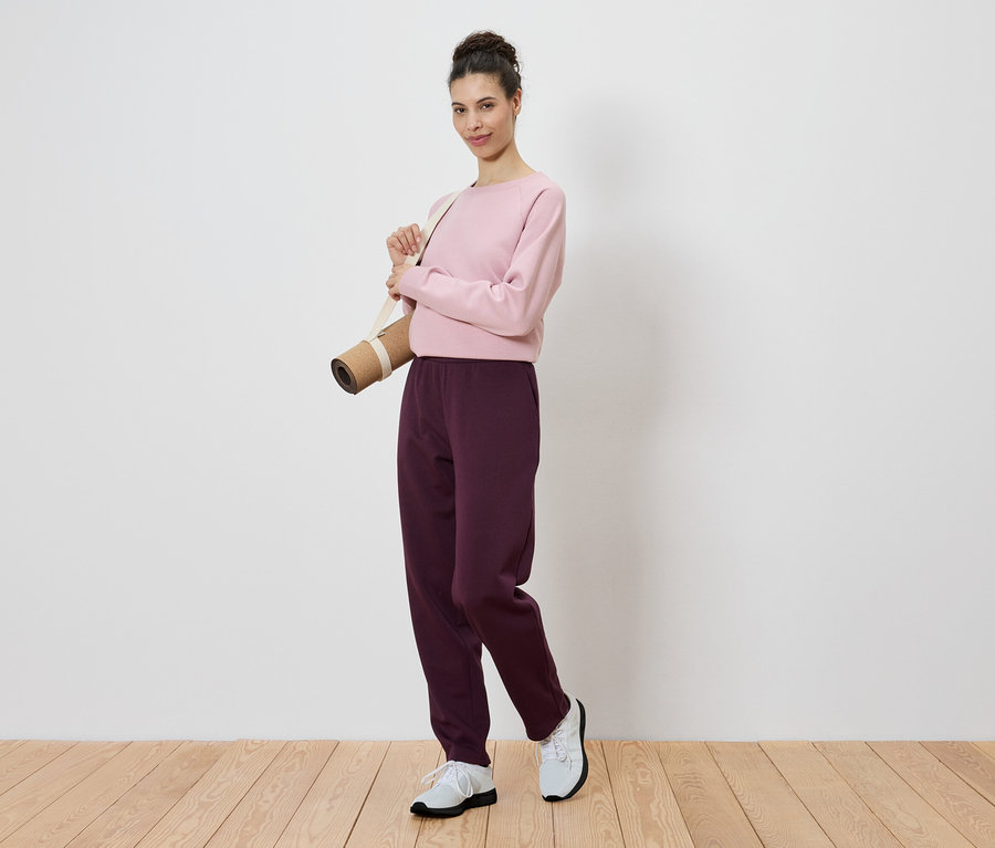 Frau mit rosa Pullover und einer Yogamatte über der Schulter.