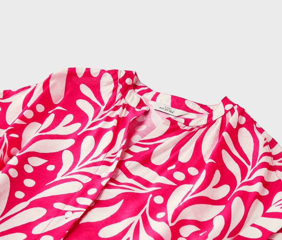 Nahaufnahme eines pinkfarbenen Blusenoberteils mit weißem Blätterdruck und V-Ausschnitt.