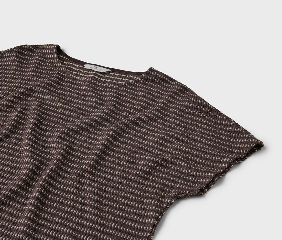 Nahaufnahme eines braunen T-Shirts mit kurzen Ärmeln und einem hellen Punktmuster auf einem grauen Hintergrund.