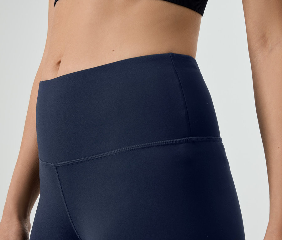 Nahaufnahme einer Frau, die marineblaue Leggings und ein schwarzes Sportoberteil trägt.