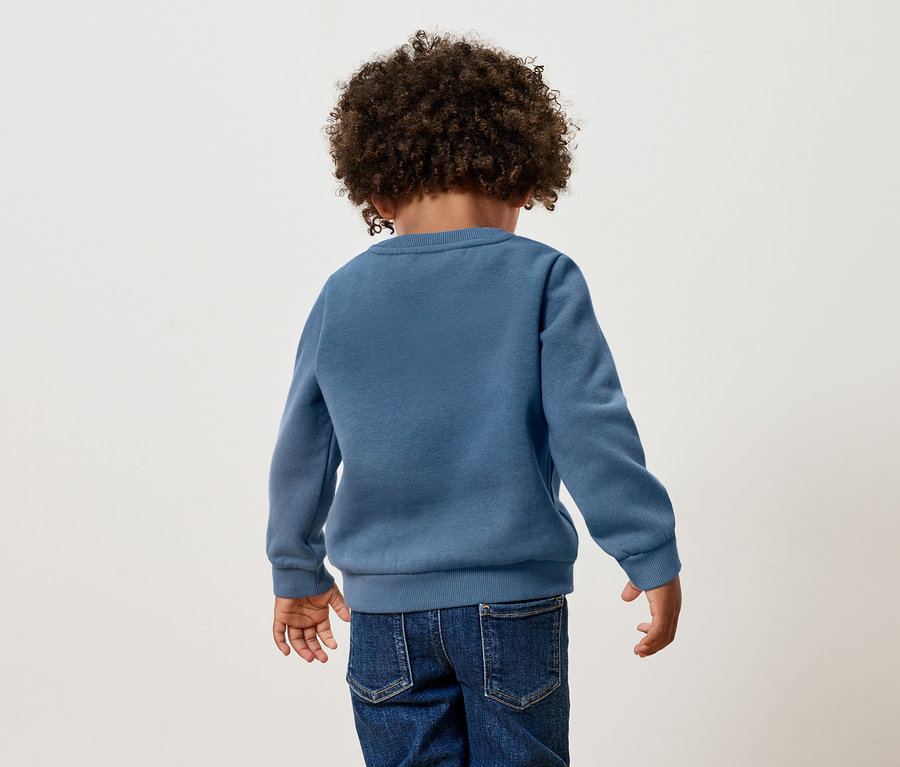Rückansicht eines Kindes mit lockigem Haar, das einen blauen Pullover und Jeans trägt.