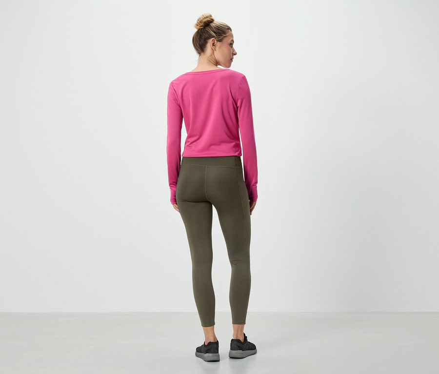 Eine Frau steht mit dem Rücken zur Kamera und trägt ein pinkes Langarmshirt und olivgrüne Leggings.