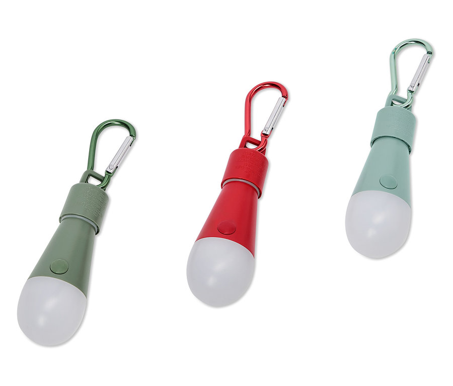 Drei farbige LED-Lampen mit Karabinerhaken liegen auf einem weißen Hintergrund.