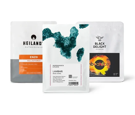Drei Kaffeepackungen des "Vollautomaten Probierpaket "Caffè Crema Entdecker Set" - 3x 250 g Ganze Bohne" liegen auf einem Tisch.