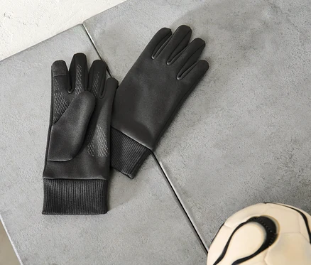 Paar schwarze Handschuhe und ein Fußball liegen auf einer grauen Oberfläche.