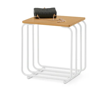 Eine schwarze, gesteppte Handtasche mit goldener Kette liegt auf einem quadratischen Beistelltisch mit heller Holzplatte und weißem Metallgestell.