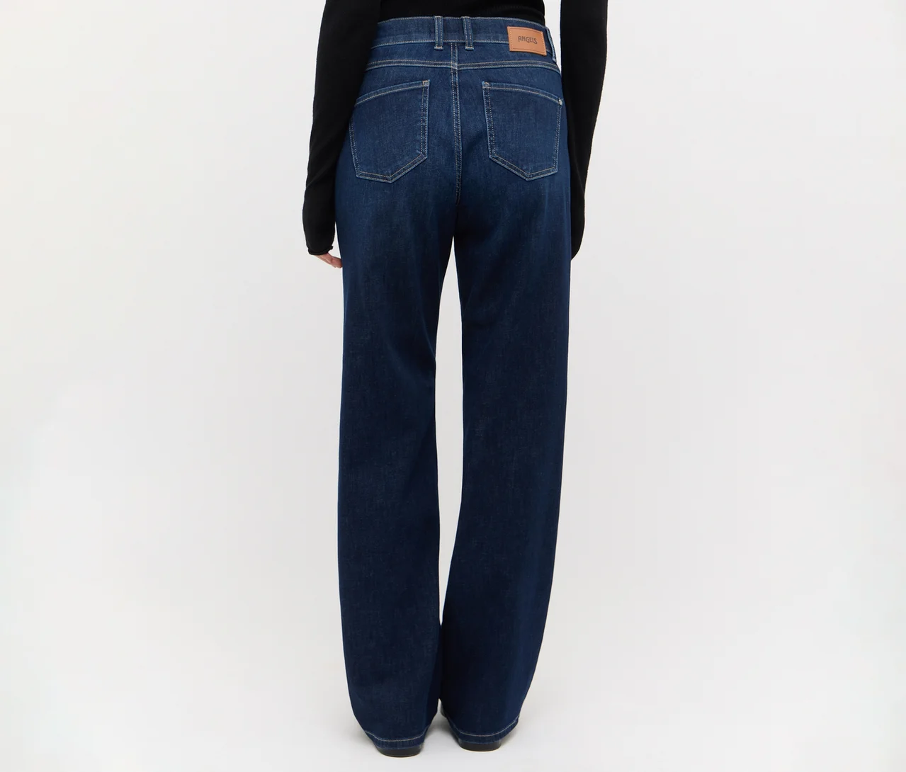 Person von hinten, trägt dunkelblaue Jeans mit weitem Bein und ein schwarzes Langarmshirt. Die Jeans hat sichtbare Gesäßtaschen und einen hellbraunen Aufnäher am Bund.