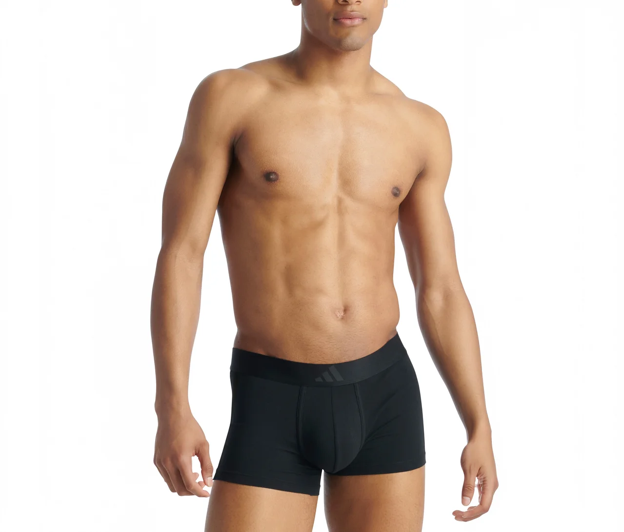 Oberkörperfreier Mann mit dunklerem Teint trägt schwarze Boxershorts mit sichtbarem Adidas-Logo am Bund, stehend vor weißem Hintergrund.