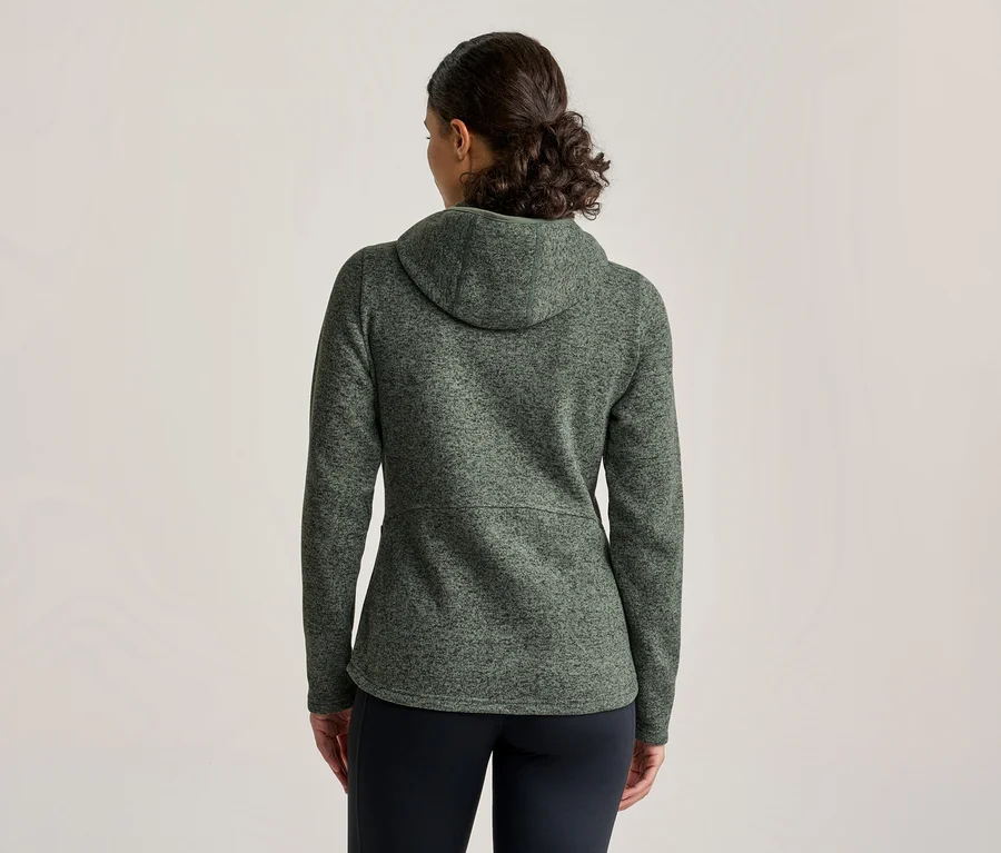 Frau von hinten, trägt eine grüne, melierte Kapuzenjacke und schwarze Hose.