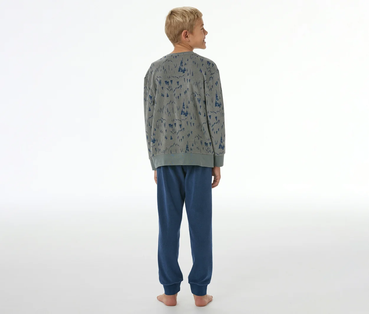 Junge von hinten in grauem SCHIESSER Kinder-Pyjama mit blauem Baummuster und blauer Hose mit Bündchen.