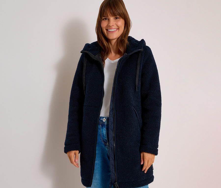 Frau lächelt und trägt eine offene, marineblaue CECIL Jacke aus Teddyfleece über einem weißen T-Shirt und Jeans.