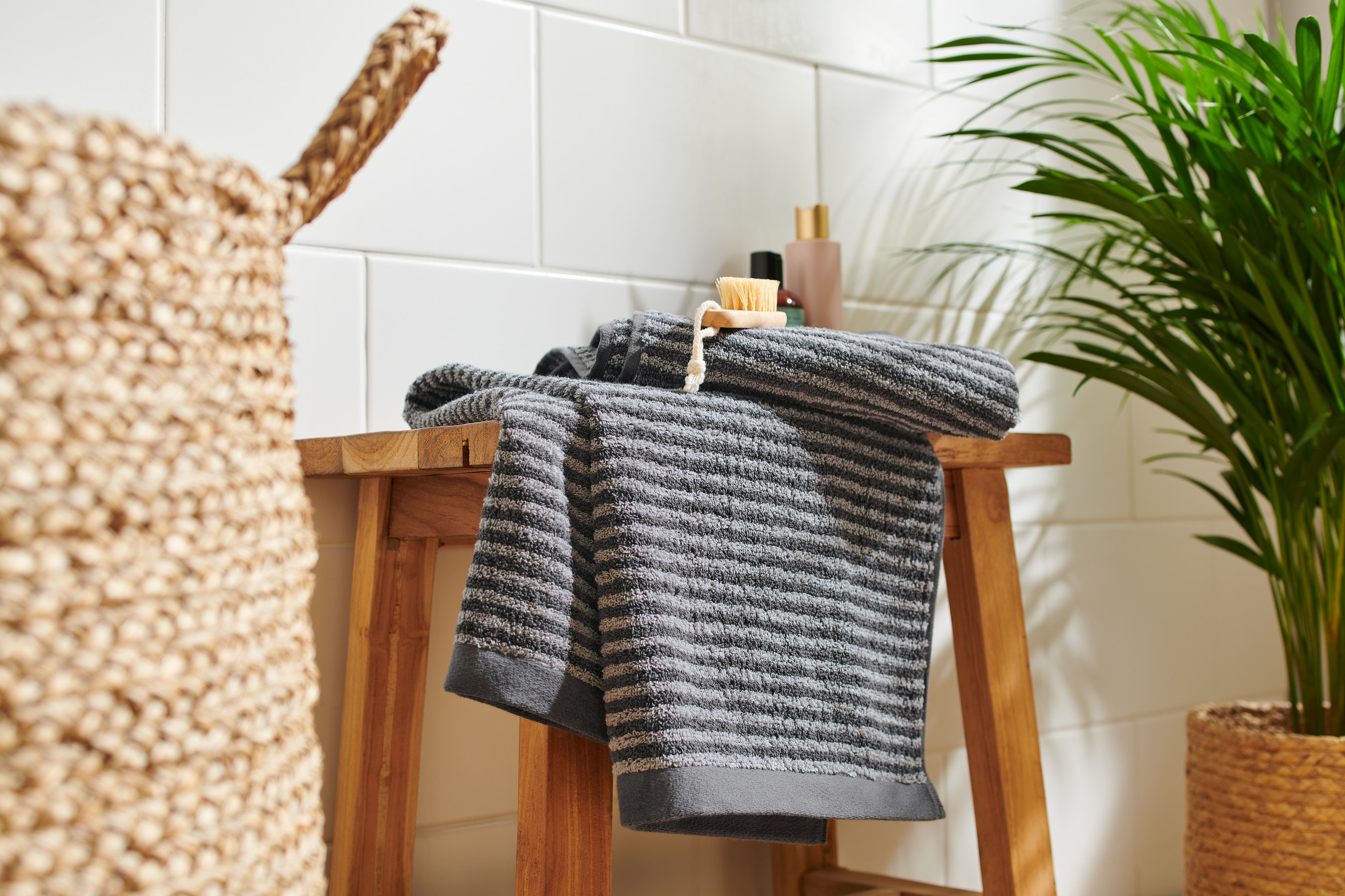 Auf einem Holzschemel liegen zwei hochwertige anthrazitfarbene Handtücher.