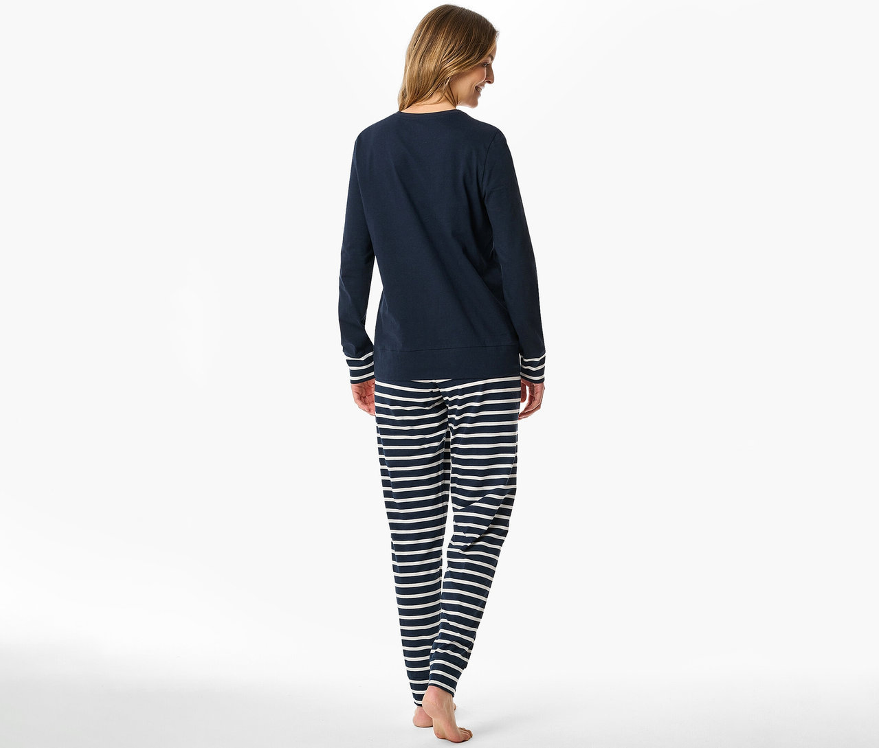 Frau von hinten in einem dunkelblauen Langarmshirt mit weiß gestreiften Bündchen und einer dunkelblau-weiß gestreiften SCHIESSER Pyjamahose.