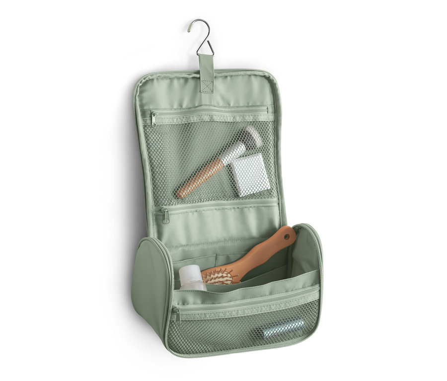 Eine offene, grüne Kulturtasche hängt an einem Haken und zeigt einen Make-up-Pinsel, Wattepads, eine Flasche und eine Haarbürste.