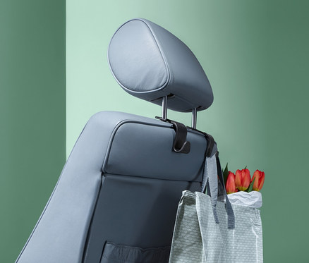 Auf der Kopfstütze eines grauen Autositzes hängen 2 Kopfstützen-Haken, an denen eine Einkaufstasche mit roten Tulpen hängt.