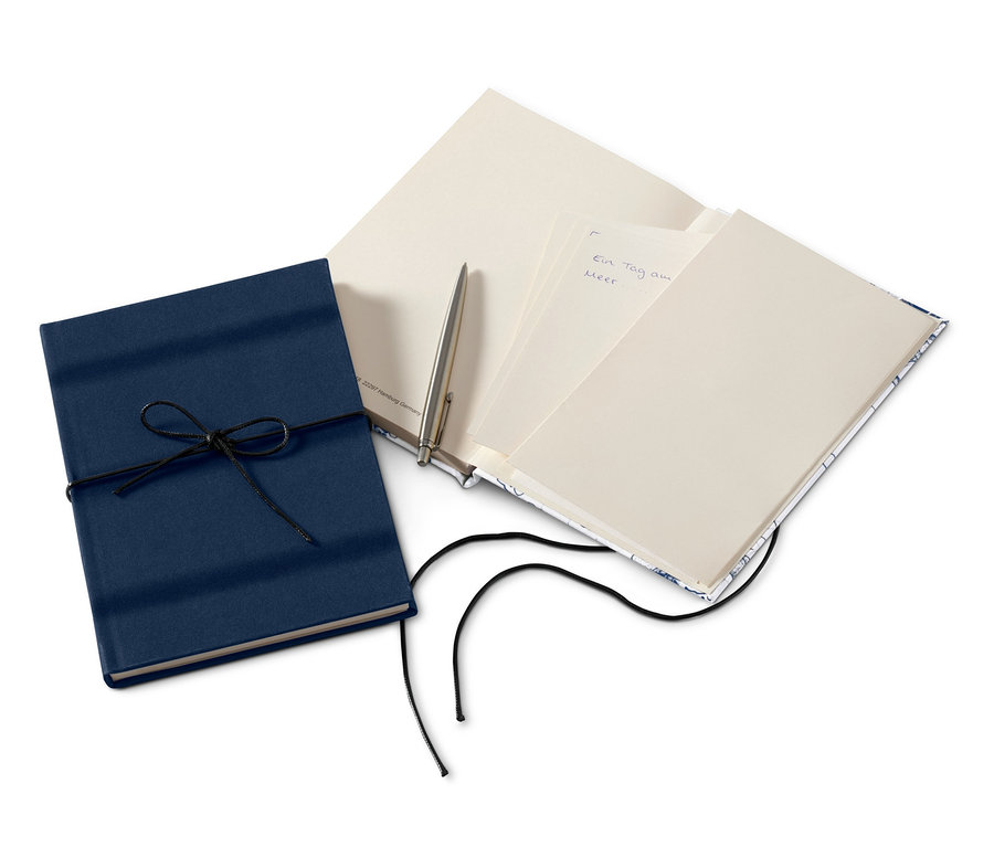 Zwei Notizbücher, eines blau mit Kordel, das andere offen mit Stift.