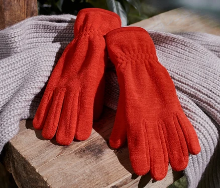 Orange Fleece-Handschuhe liegen auf einem Strickschal auf einer Holzbank.