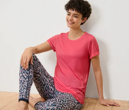 Frau sitzt auf dem Boden und trägt ein pinkes Longshirt.