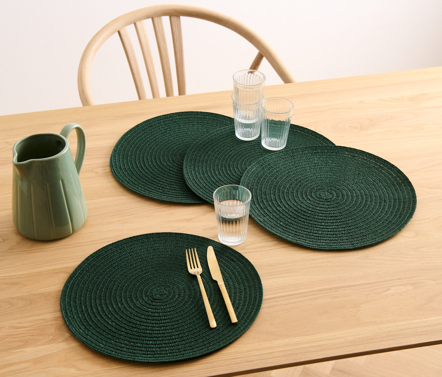 Auf einem Holztisch liegen vier grüne, runde Platzsets, ein Krug und Gläser.