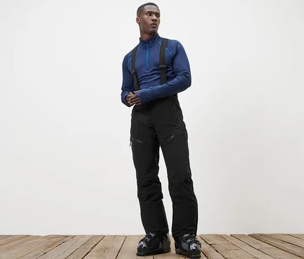 Mann steht auf Holzboden und trägt ein blaues Oberteil und eine High-Tech-Skihose.